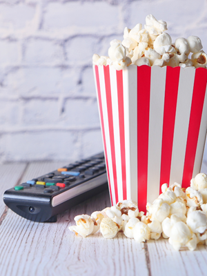 Popcorn and a remote to the left of the poprn on a white wooden floor.